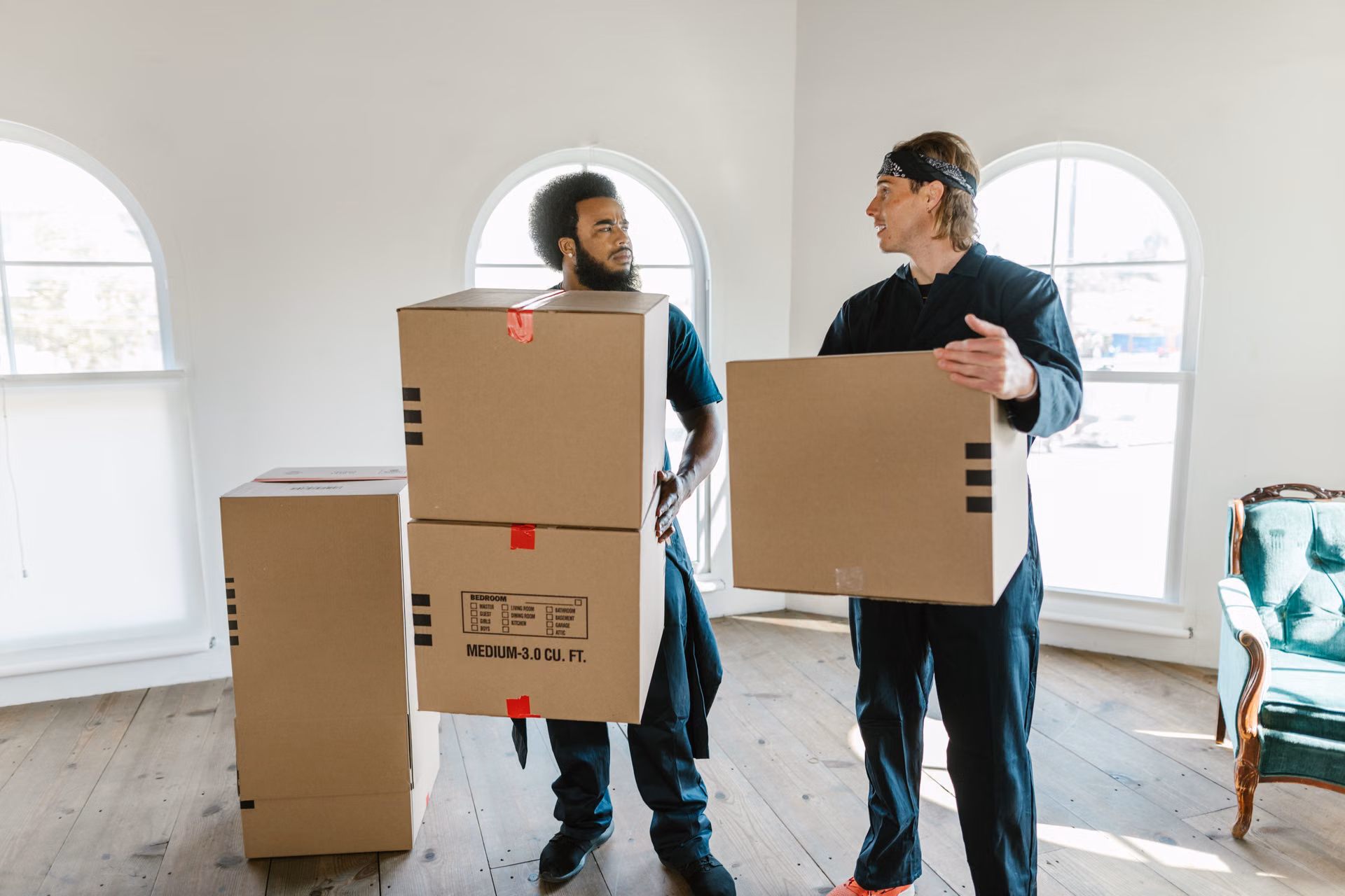 Two movers carrying boxes through a bright room