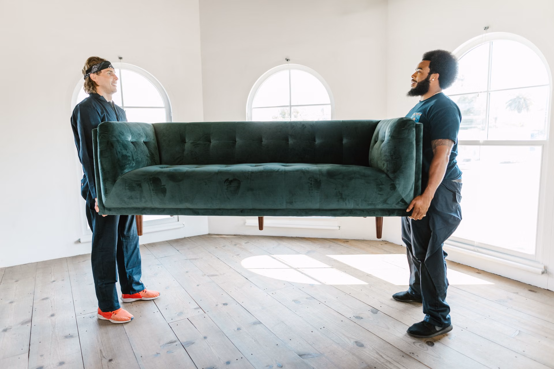 Two crew members carrying a couch out of a bright room